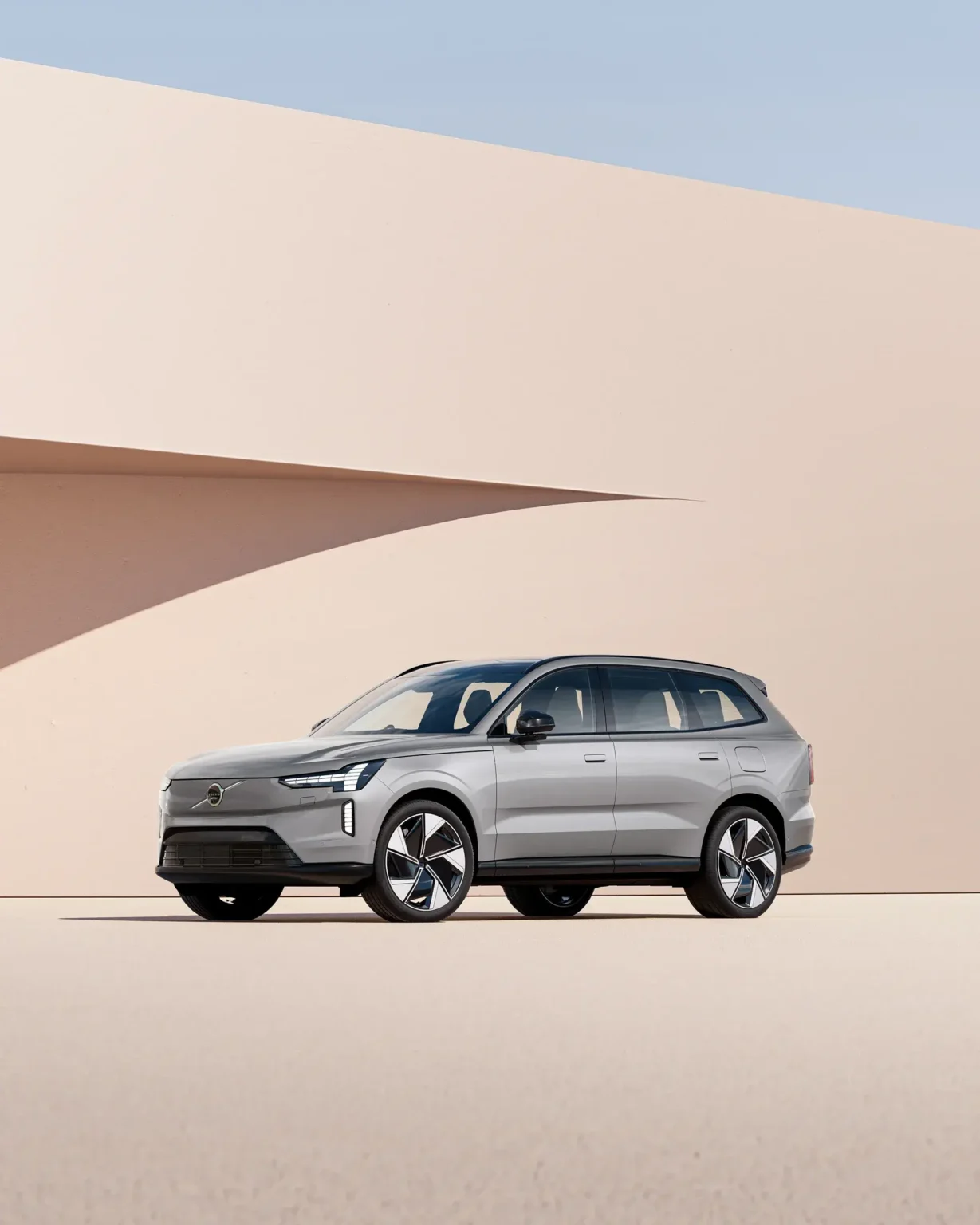 Pale grey Volvo EX90 from the front three-quarter, parked against curved sand-coloured walls