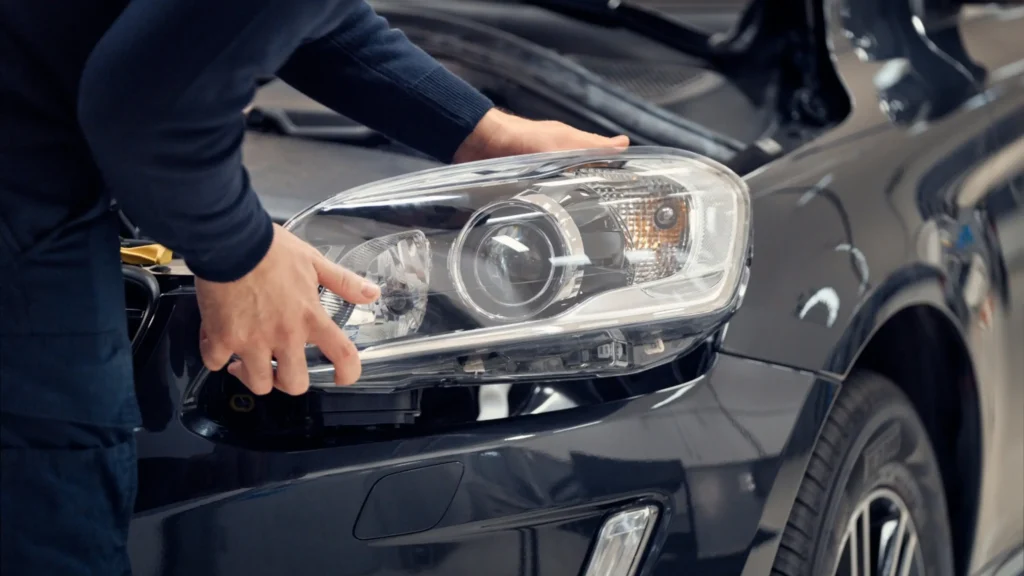 A technician's hand on the headlight of a dark grey Volvo
