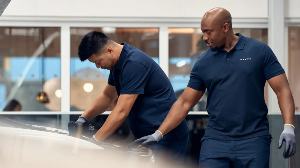 Two Volvo service technicians in navy uniforms working on a white Volvo in the workshop