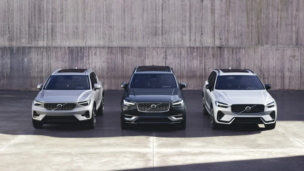 Three Volvo SUVs in silver, dark grey and white parked side by side in front of a concrete wall