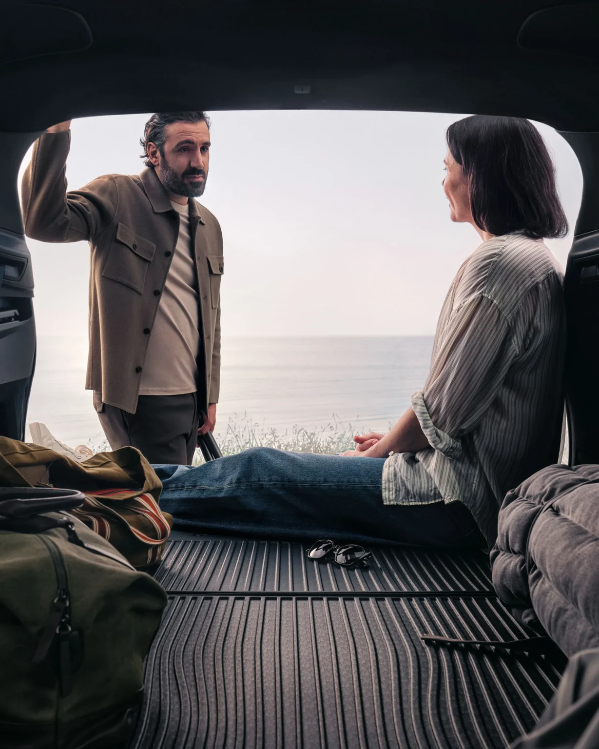 A woman sitting in the open boot of a Volvo XC90 as a man leans in, with bags on the load floor
