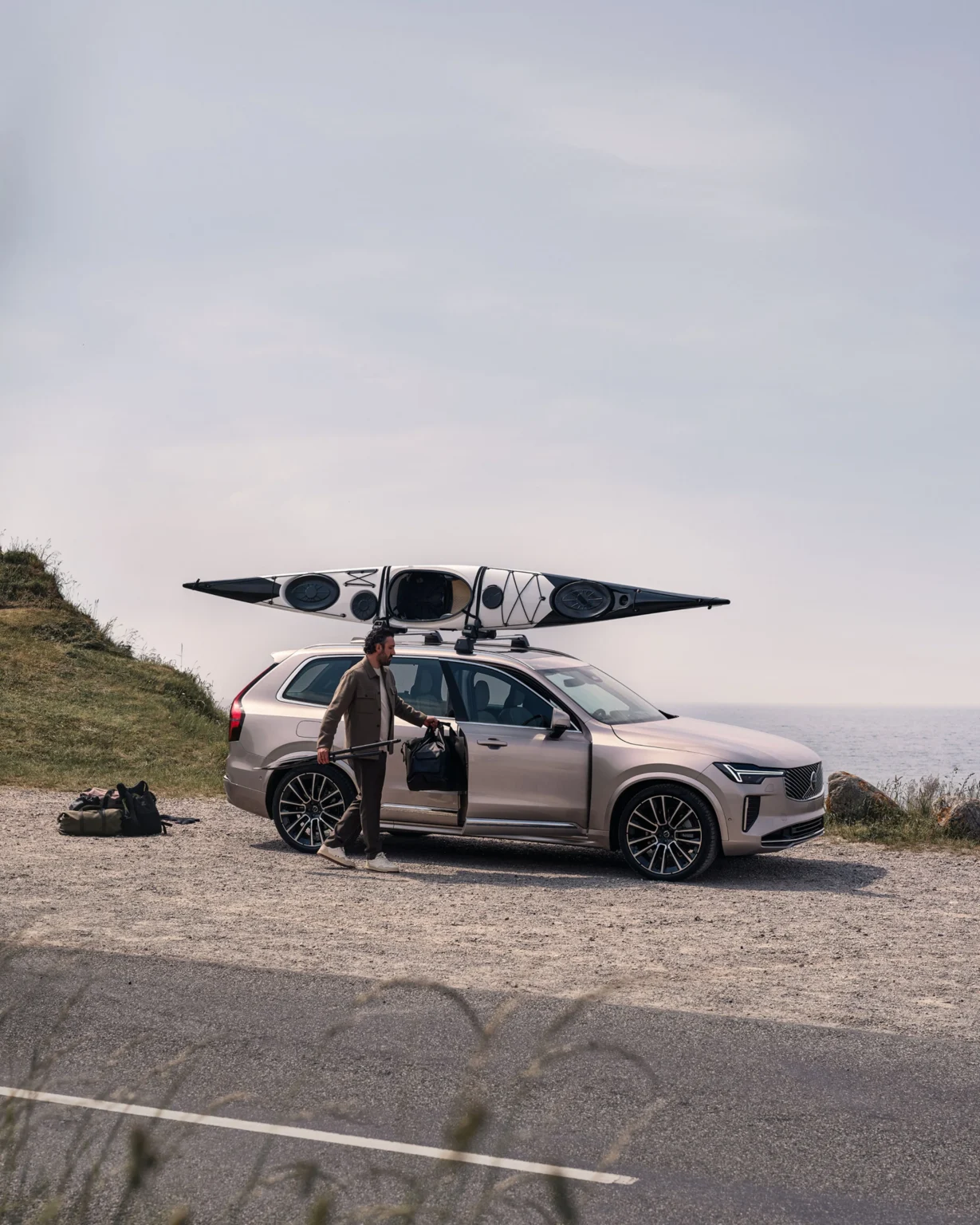Volvo XC90 with two kayaks on its roof, parked on a gravel clifftop by the sea