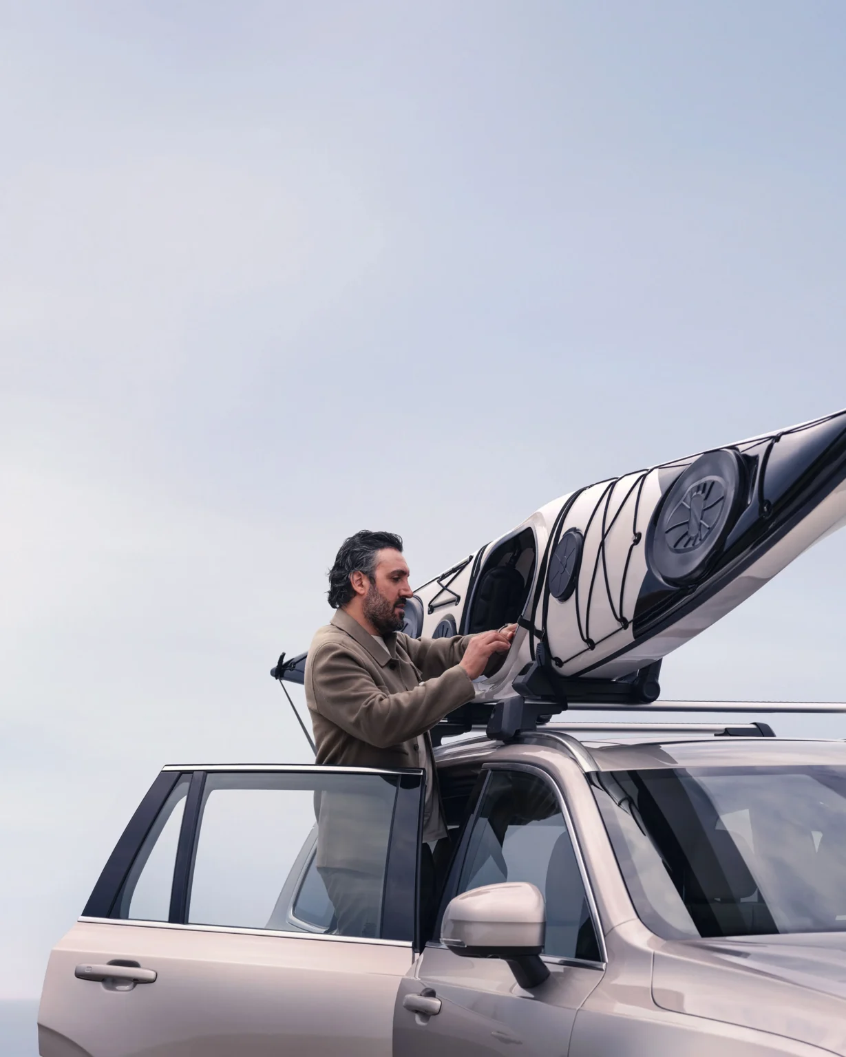 A man fastening kayaks to the roof rack of a Volvo XC90, standing in its open doorway