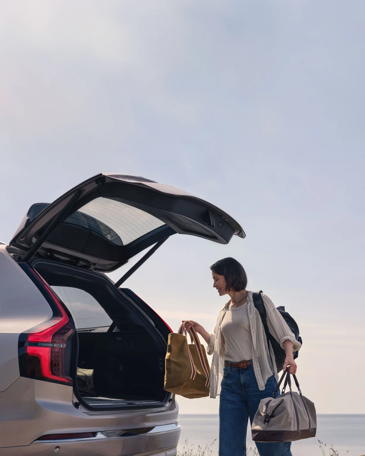 A woman loading bags into the open boot of a Volvo XC90