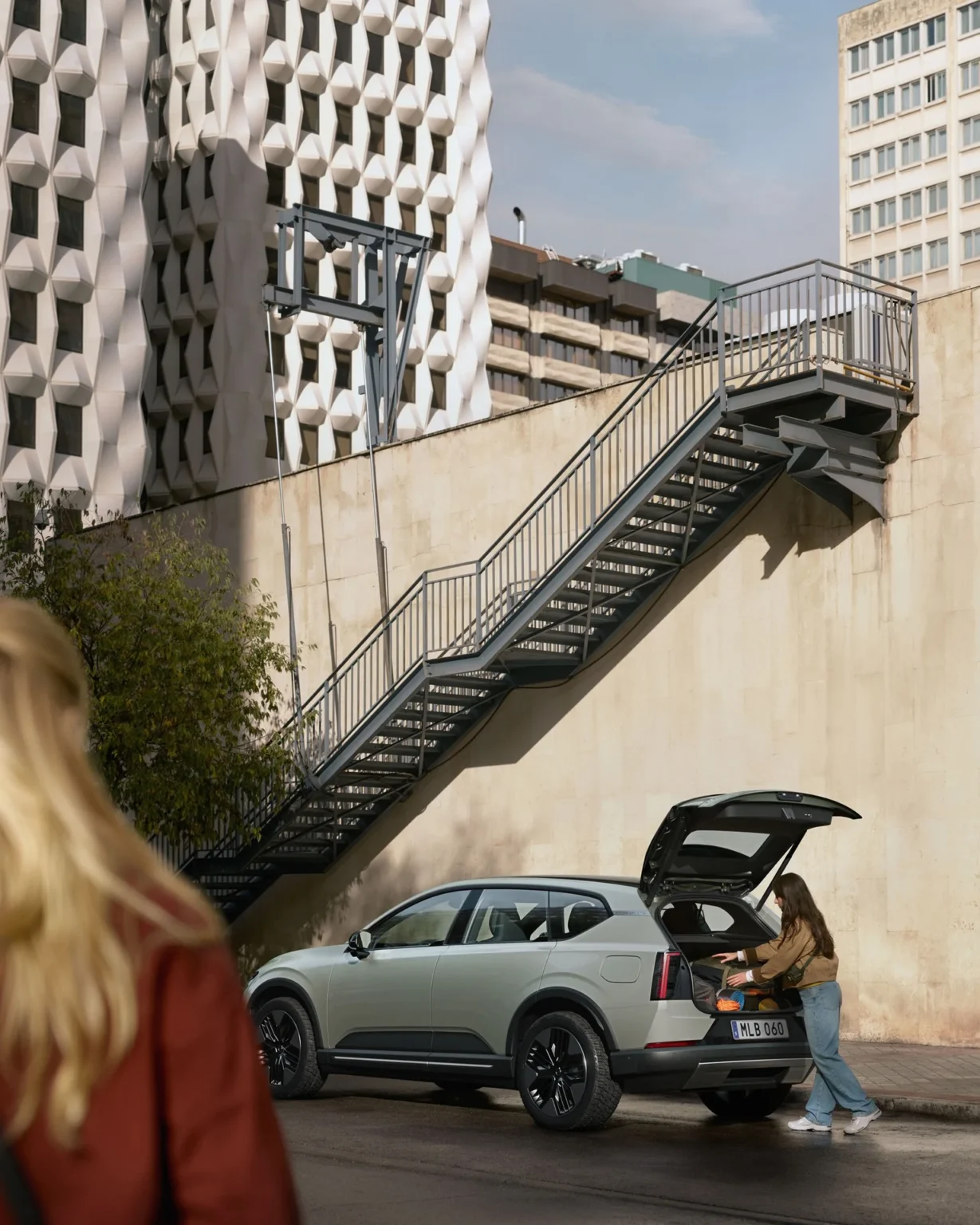 Person loading the boot of a Volvo EX60 Cross Country with the tailgate open on a city street