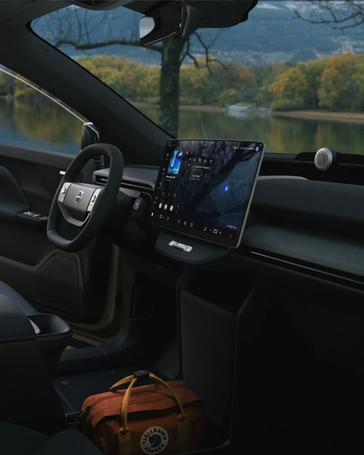 Interior of a Volvo EX60 Cross Country seen through the open passenger door, with a lake outside