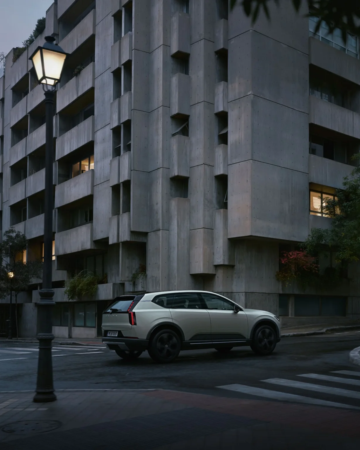 Volvo EX60 Cross Country on a city street corner beside a concrete apartment building at dusk