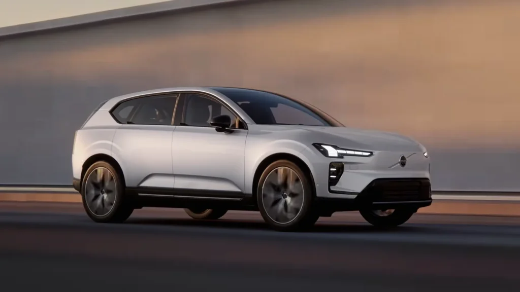 Volvo EX60 in Crystal White driving past a wall at dusk