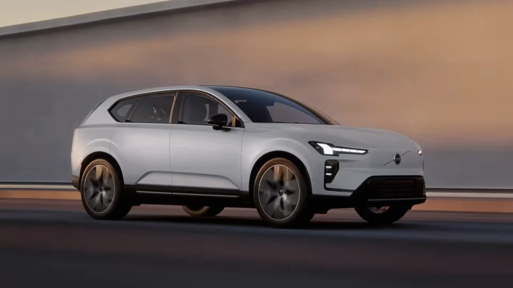 Volvo EX60 in Ice White driving past a wall at dusk