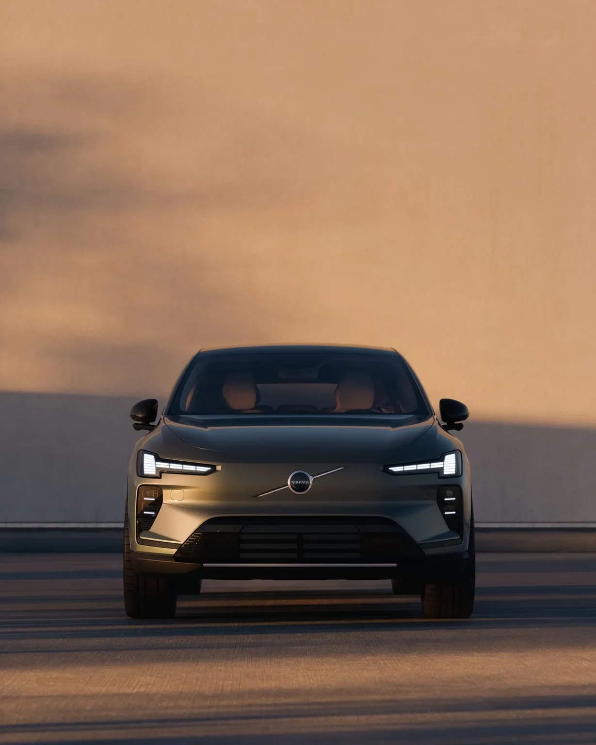 Front view of a Volvo EX60 with its headlights on at dusk