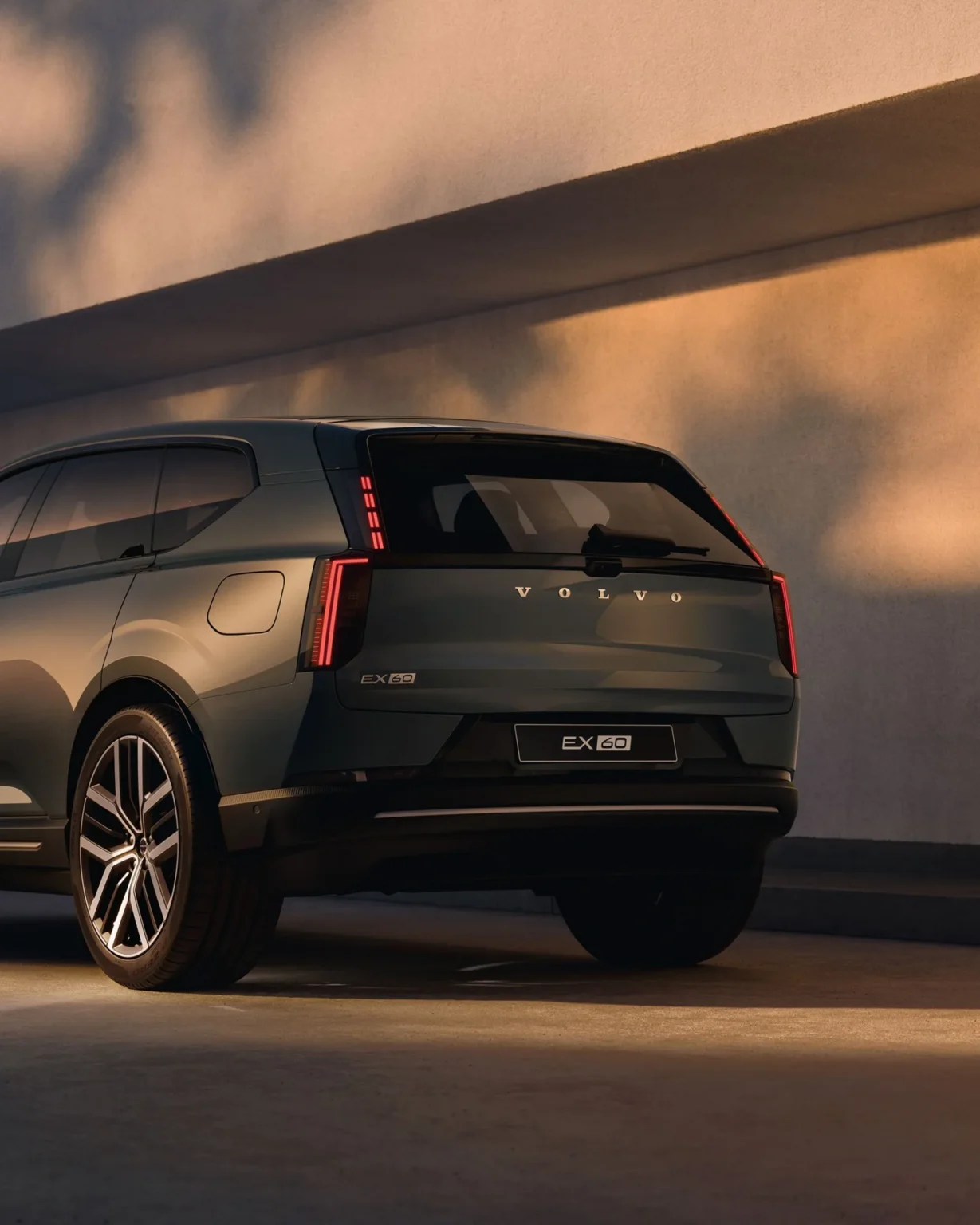 Volvo EX60 rear three-quarter view against a wall at dusk