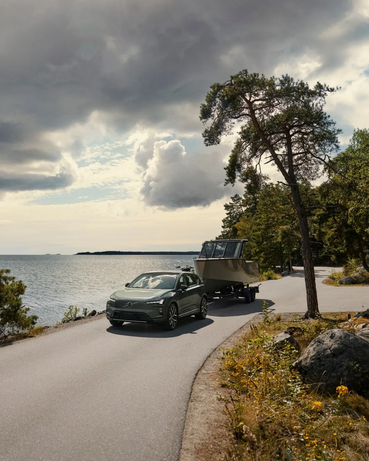 Volvo EX60 towing a boat on a coastal road