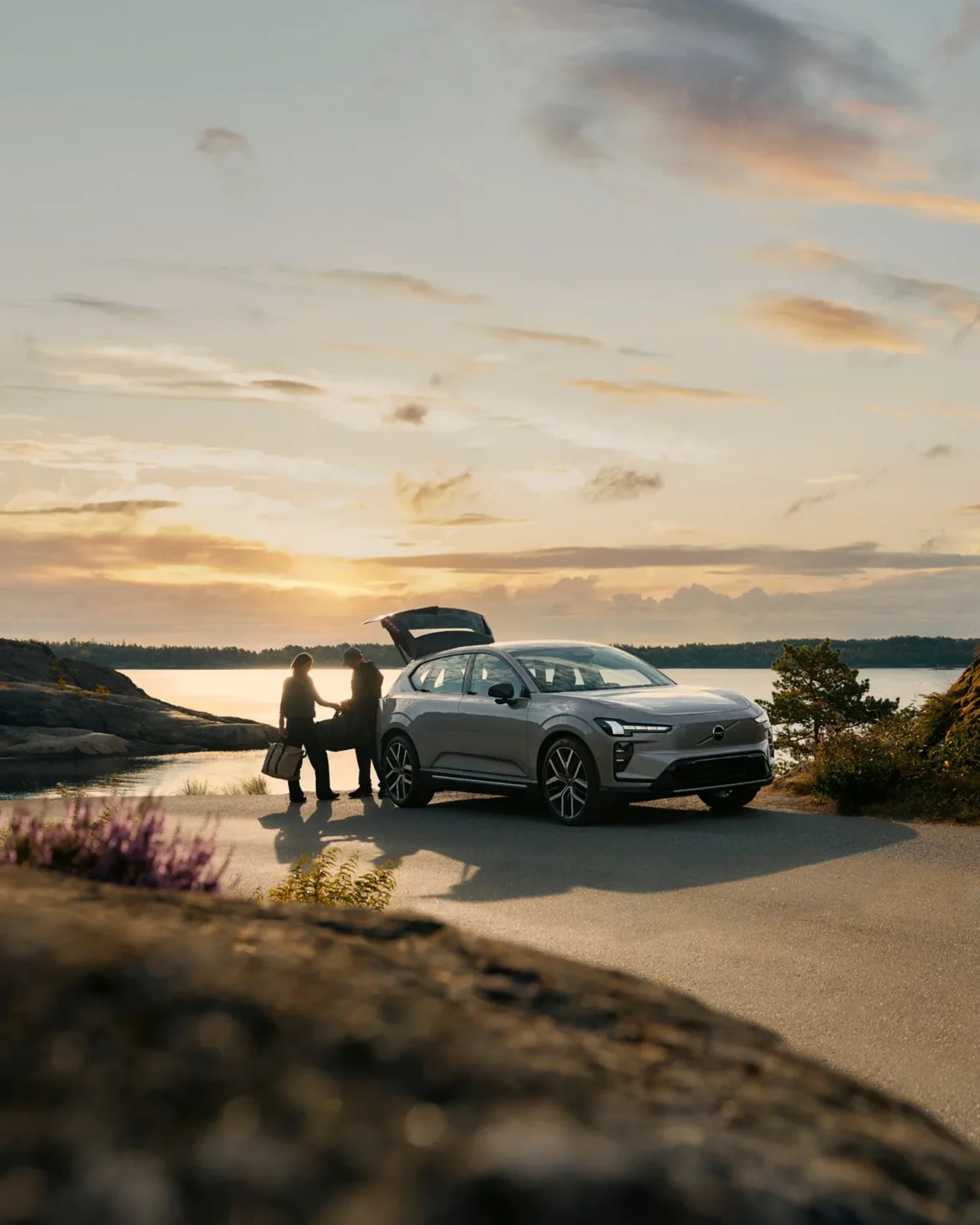 Volvo EX60 parked by the coast at sunset while two people unload gear