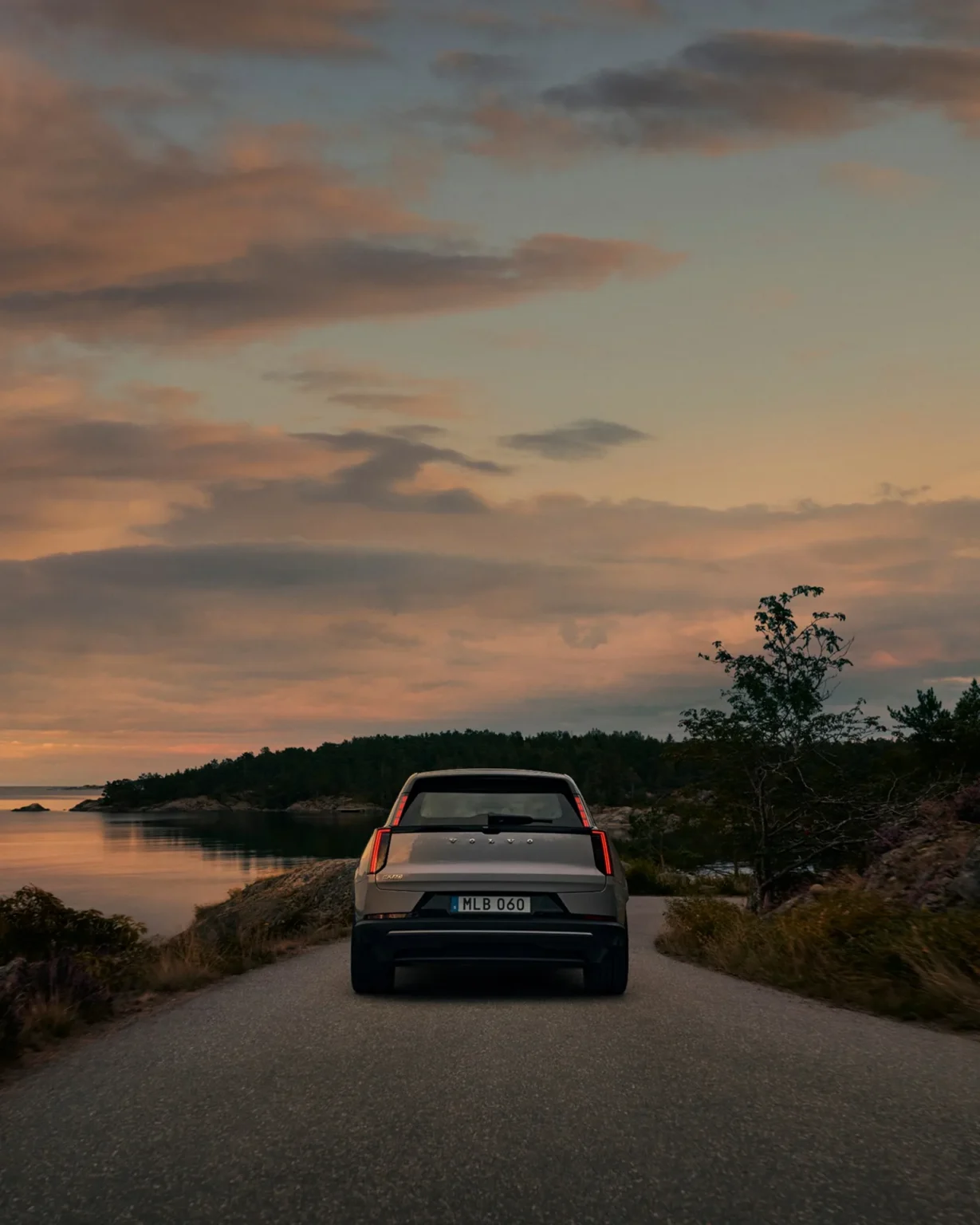 Rear of a Volvo EX60 driving along a coastal road at dusk