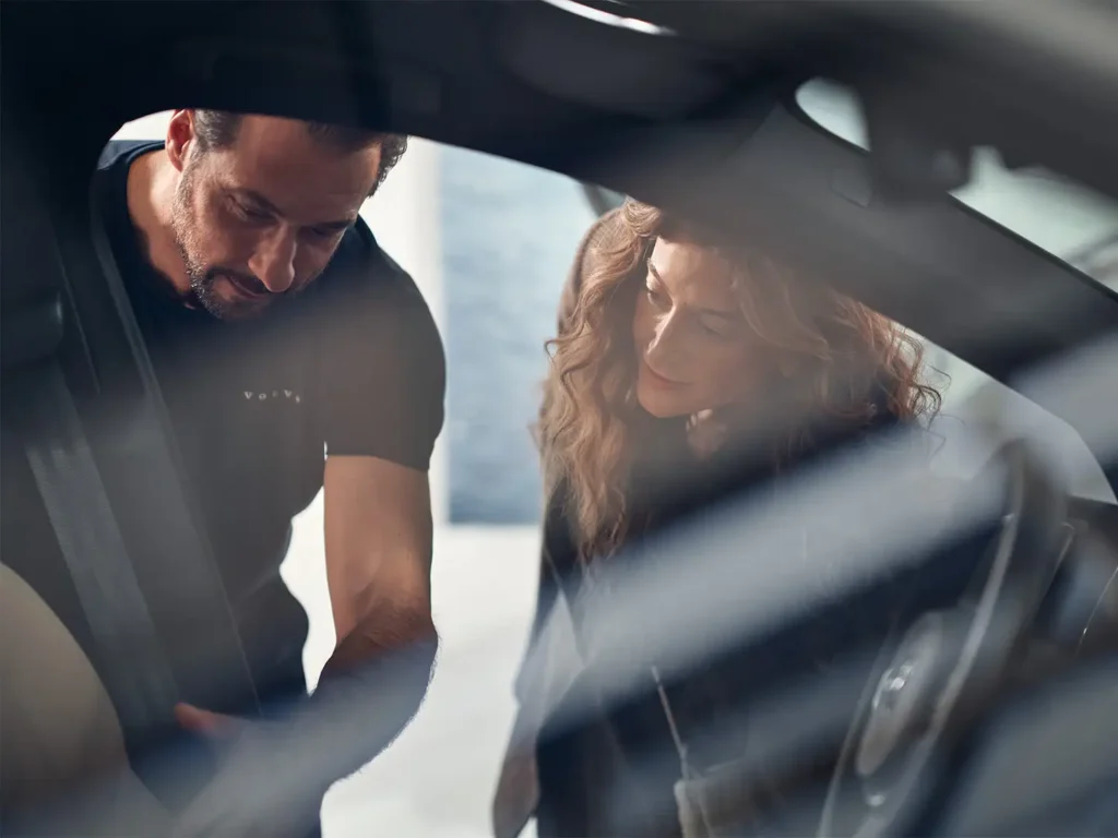 A Volvo technician leaning into a car to talk to the woman in the driver’s seat