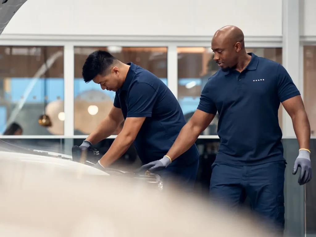 Two Volvo technicians in navy shirts working on the front of a car