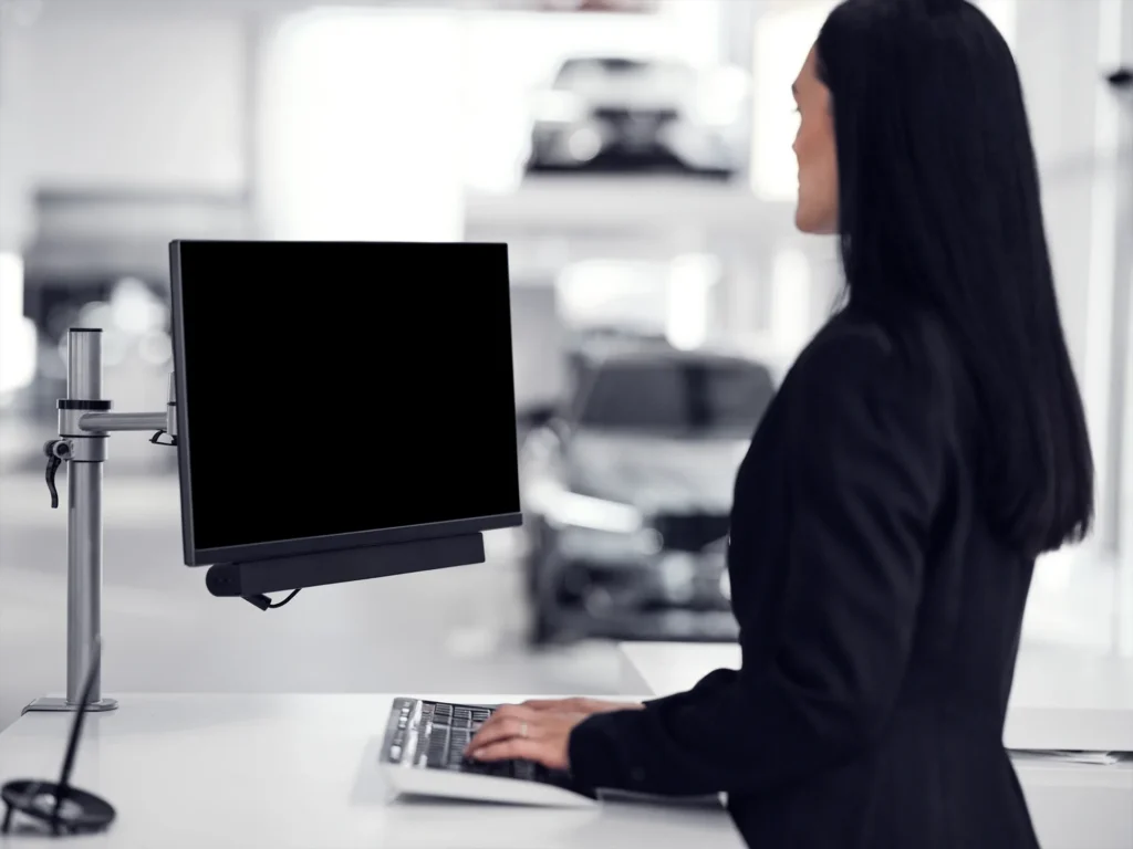 A woman in a black jacket typing at a computer at a desk in a Volvo showroom