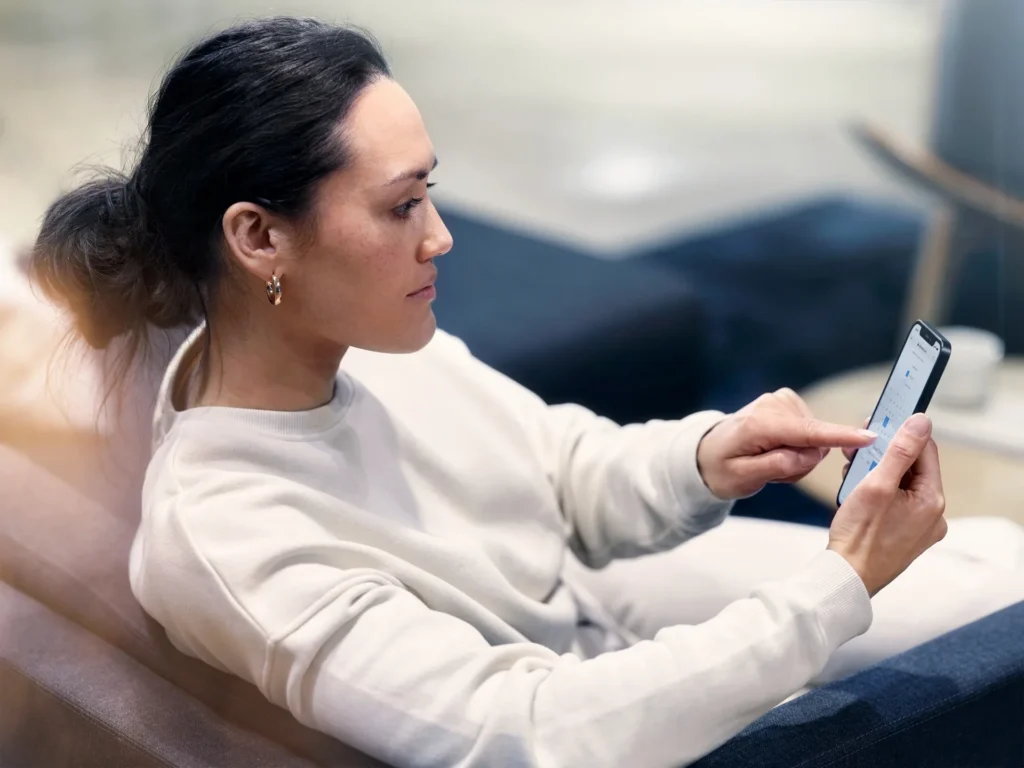A woman in a white jumper on a sofa, tapping on her phone