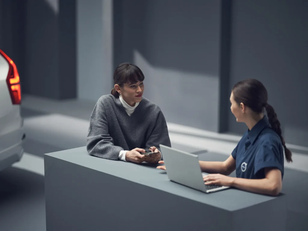 A customer talking to a Volvo staff member working on a laptop at a desk in a showroom