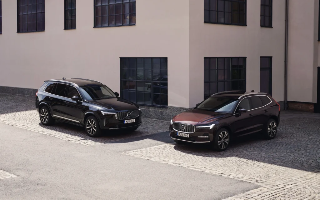 A black Volvo XC90 and a dark red Volvo XC60 parked on cobblestones outside a pale building