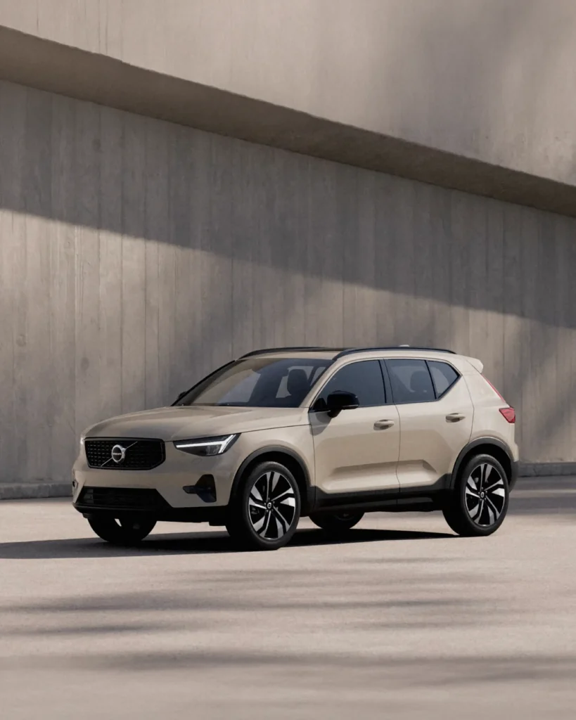 A sand-coloured Volvo XC40 with a black roof, parked in front of a board-marked concrete wall in sun and shade