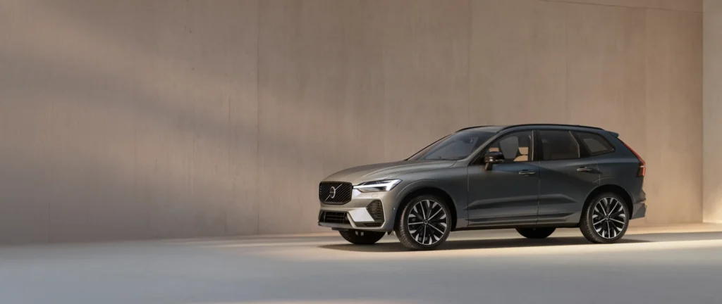 A dark grey Volvo XC60 parked in front of a warm beige wall in soft, low sunlight