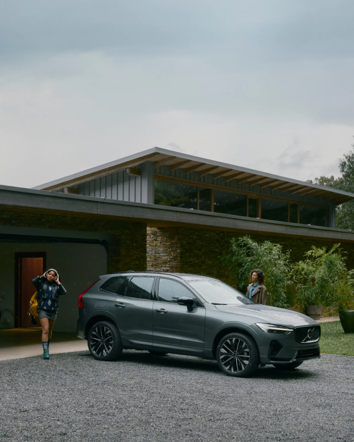 Two women with bags walking to a Volvo XC60 parked outside a modern house