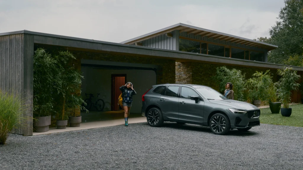 A dark grey Volvo XC60 on the gravel drive of a modern house, two women walking to it with their bags