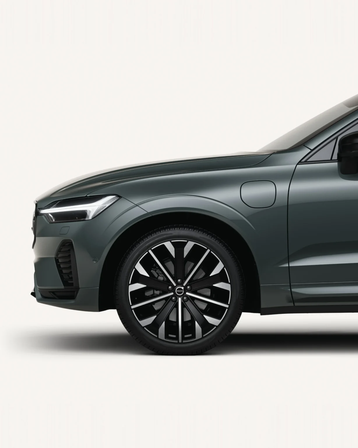 Front half of a Volvo XC60 Plug-in Hybrid in a white studio, showing its front wheel and charging flap