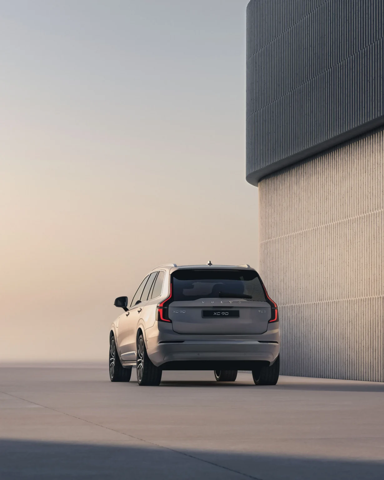 Volvo XC90 from the rear, parked beside a tall ribbed concrete wall at dusk