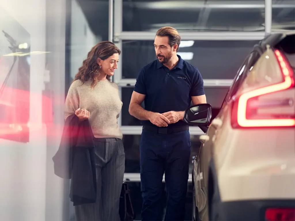A Volvo technician talking with a woman beside a white Volvo in the workshop