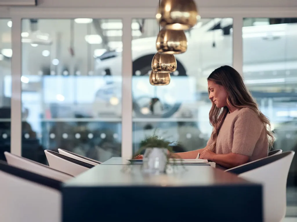 A woman working on her laptop at a table in a Volvo showroom